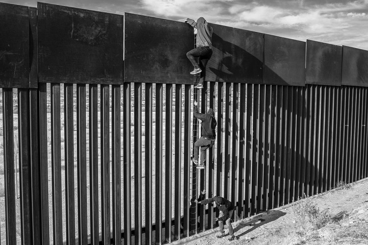 Na fotografiji su migranti koji uz pomoć ljestvi se penju na zid, a u svemu im pomažu krijumčari. 