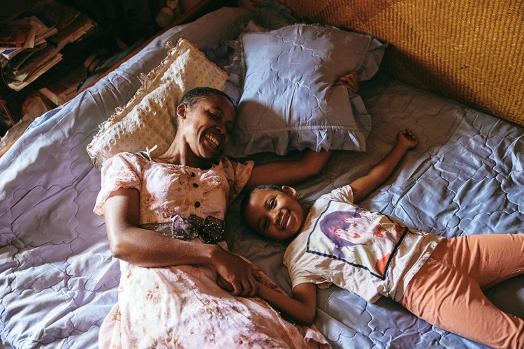 Na fotografiji se nalazi Džoelina (41) sa petogodišnjom ćerkom kako leže na krevetu, a svoj dom dijele sa Dada Paulom (91) koji boluje od demencije. Džoelina je jedini hranitelj ove porodice. 